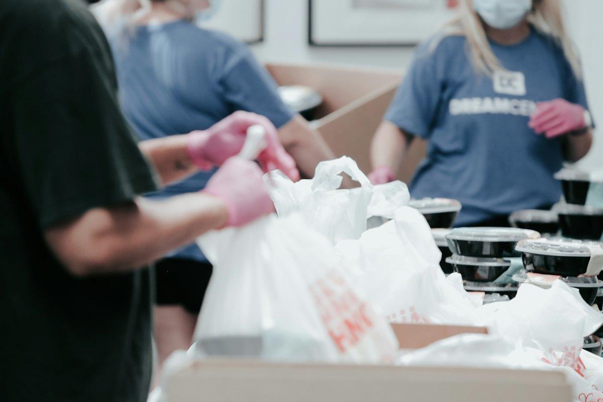 Volunteers pack meals into bags at a food distribution table.