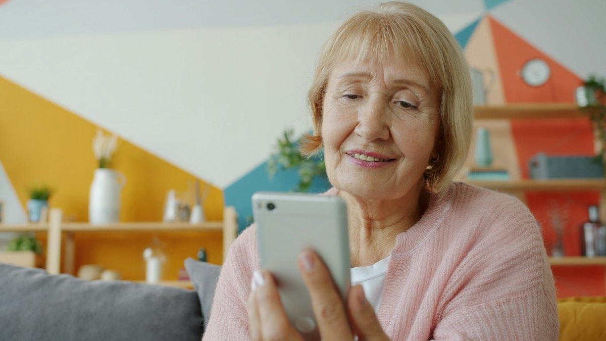 An older woman smiles at a message on her phone.
