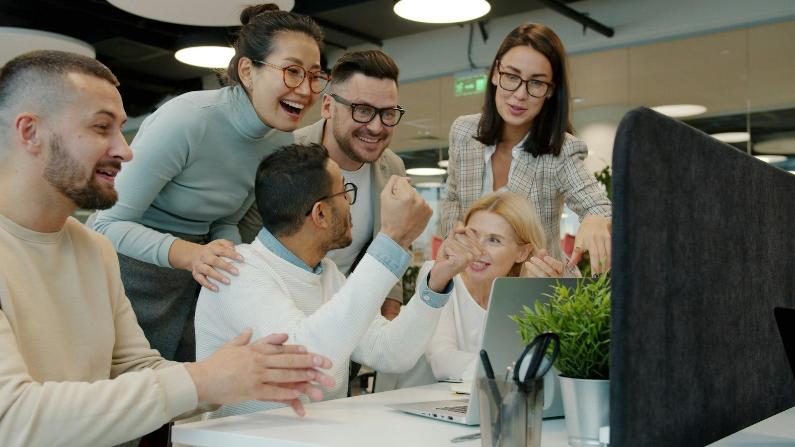 Colleagues cheering together around a laptop in an office