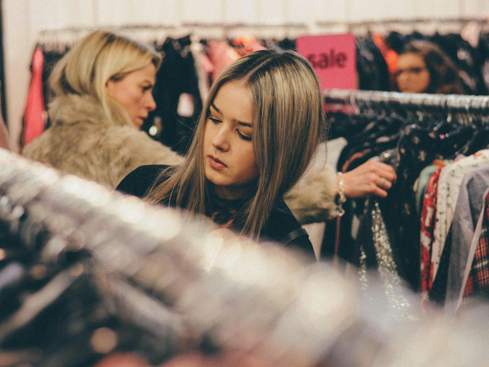 Two young women browsing racks of clothes in a store