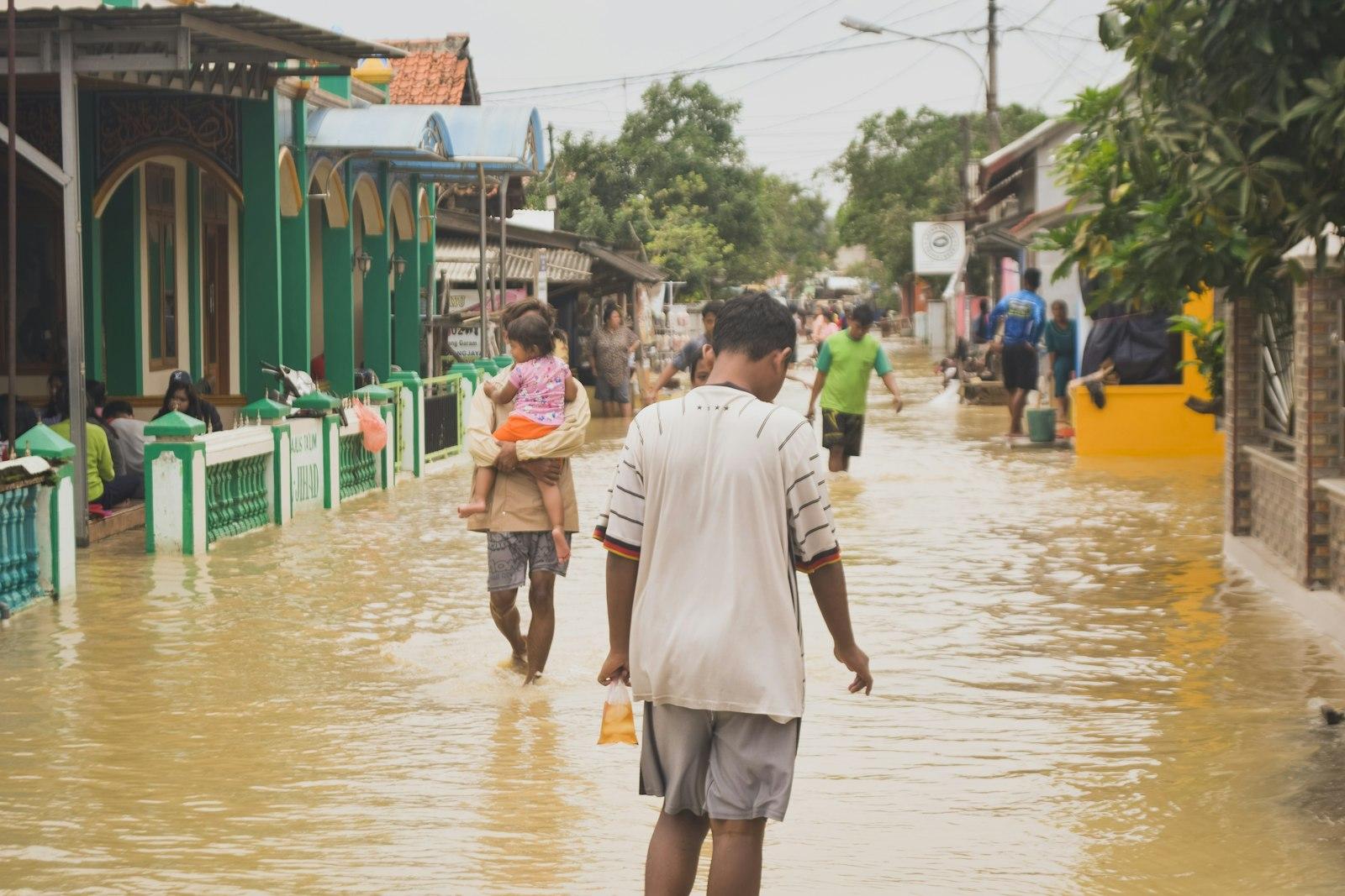 A father carrying his child through a flooded neighbourhood street